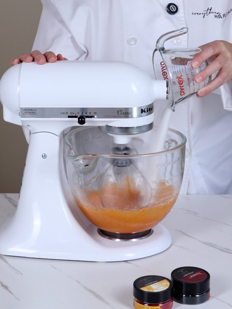 Mixing bowl of a stand mixer with egg whites and food coloring.