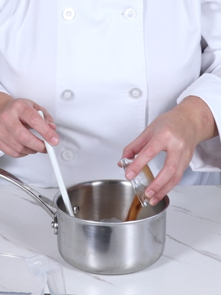 Hands are adding cinnamon powder into the saucepan.