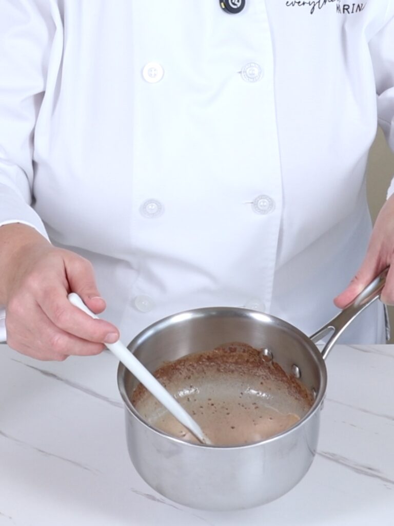 Hands are holding a saucepan and a spatula.