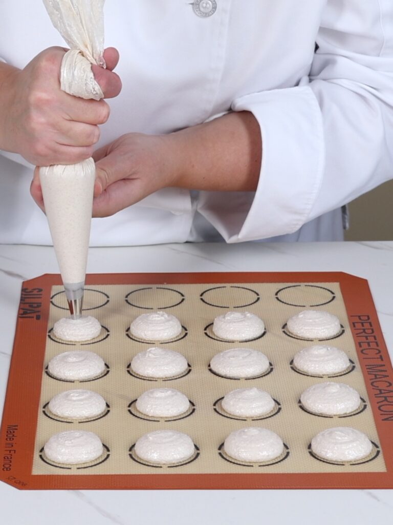 Hands are piping macarons.