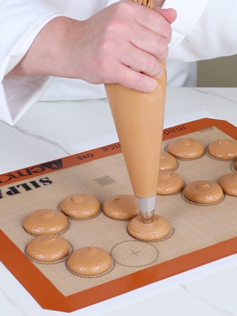 Hand is piping a macaron wreath on the mat.