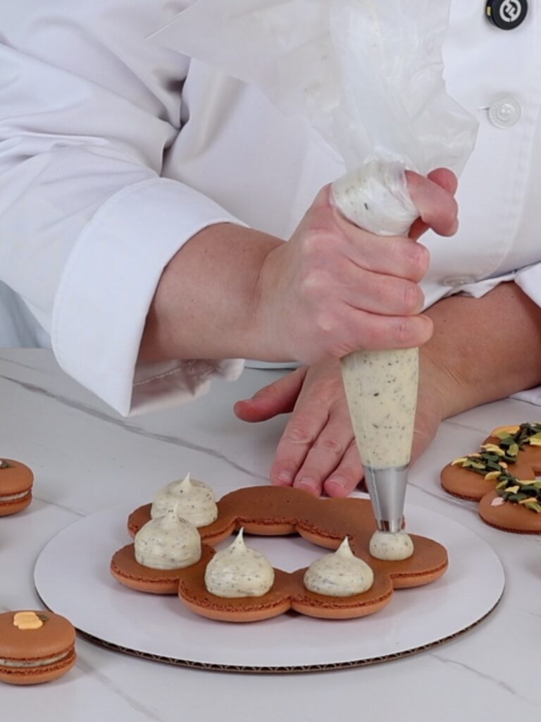 Hand is piping chai filling on the macaron wreath.