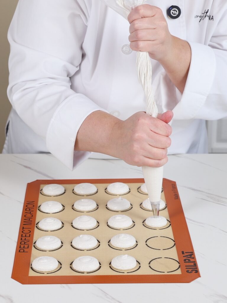 Hands are piping white macarons.