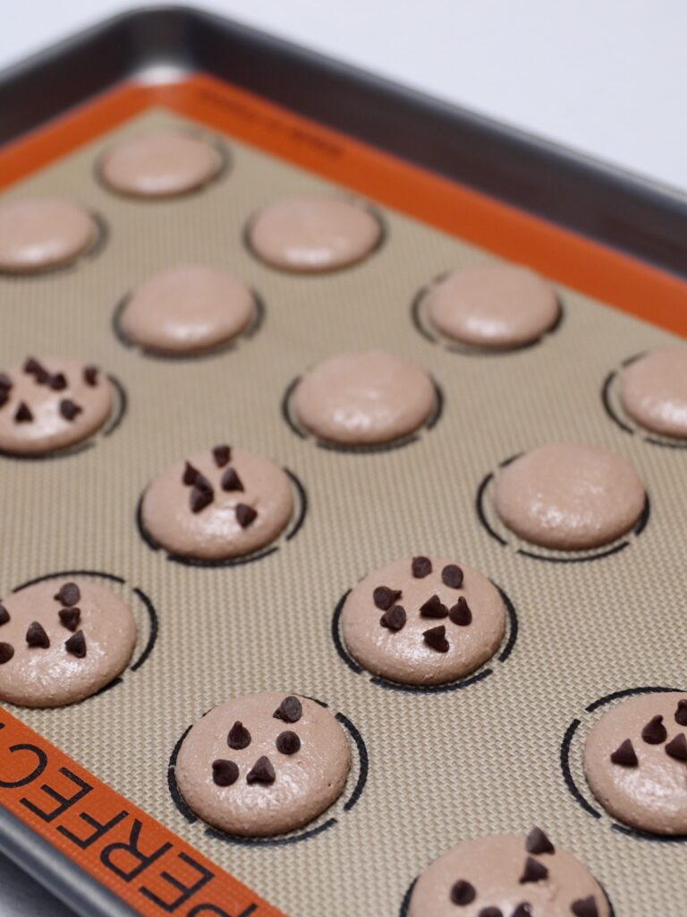 Chocolate macarons topped with chocolate chips. 