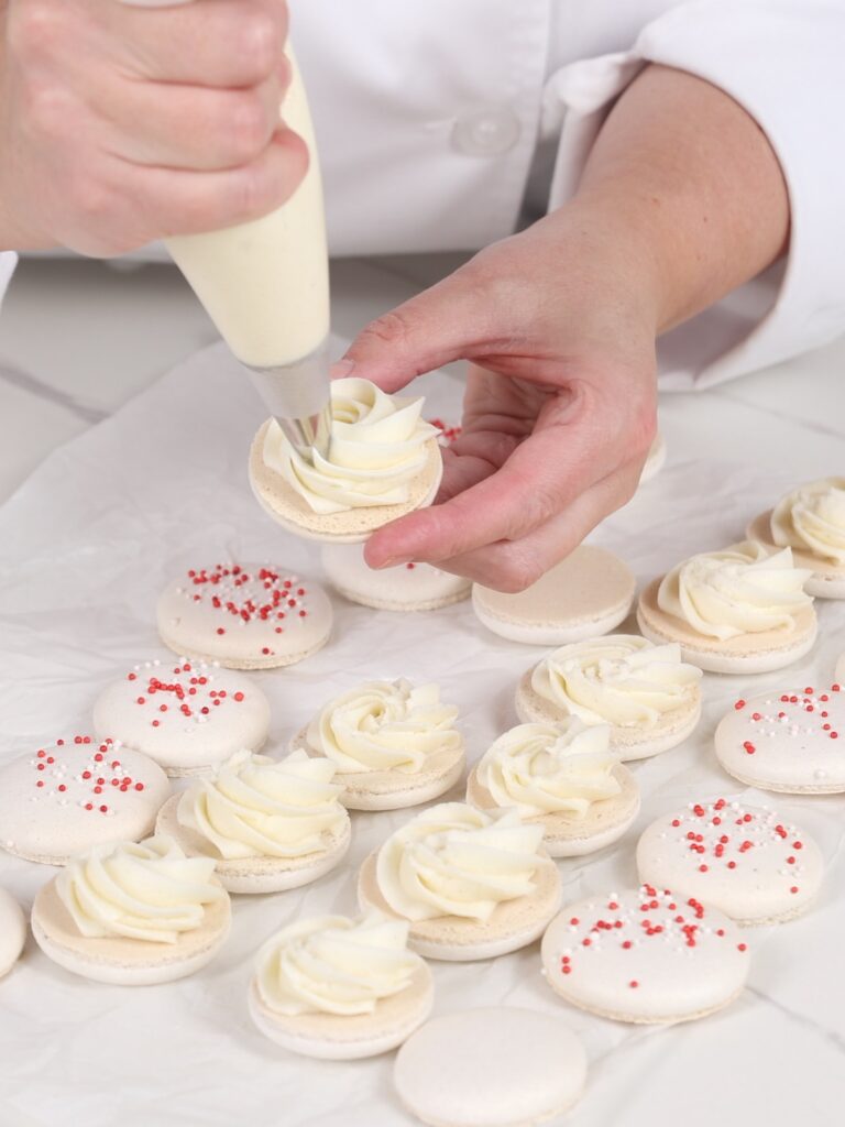 Piping ermine buttercream on the macaron shell.