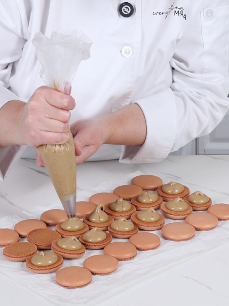 Piping gingerbread latte ganache on the macaron shells. 