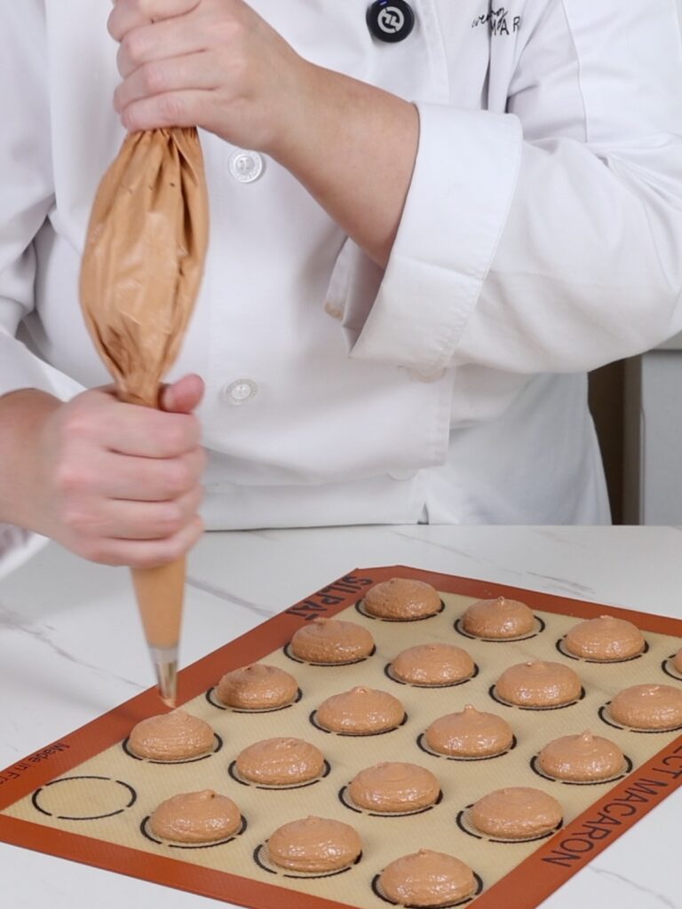 Piping macarons on the mat. 