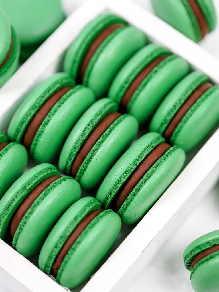 Green macarons filled with dark chocolate ganache in the box. 