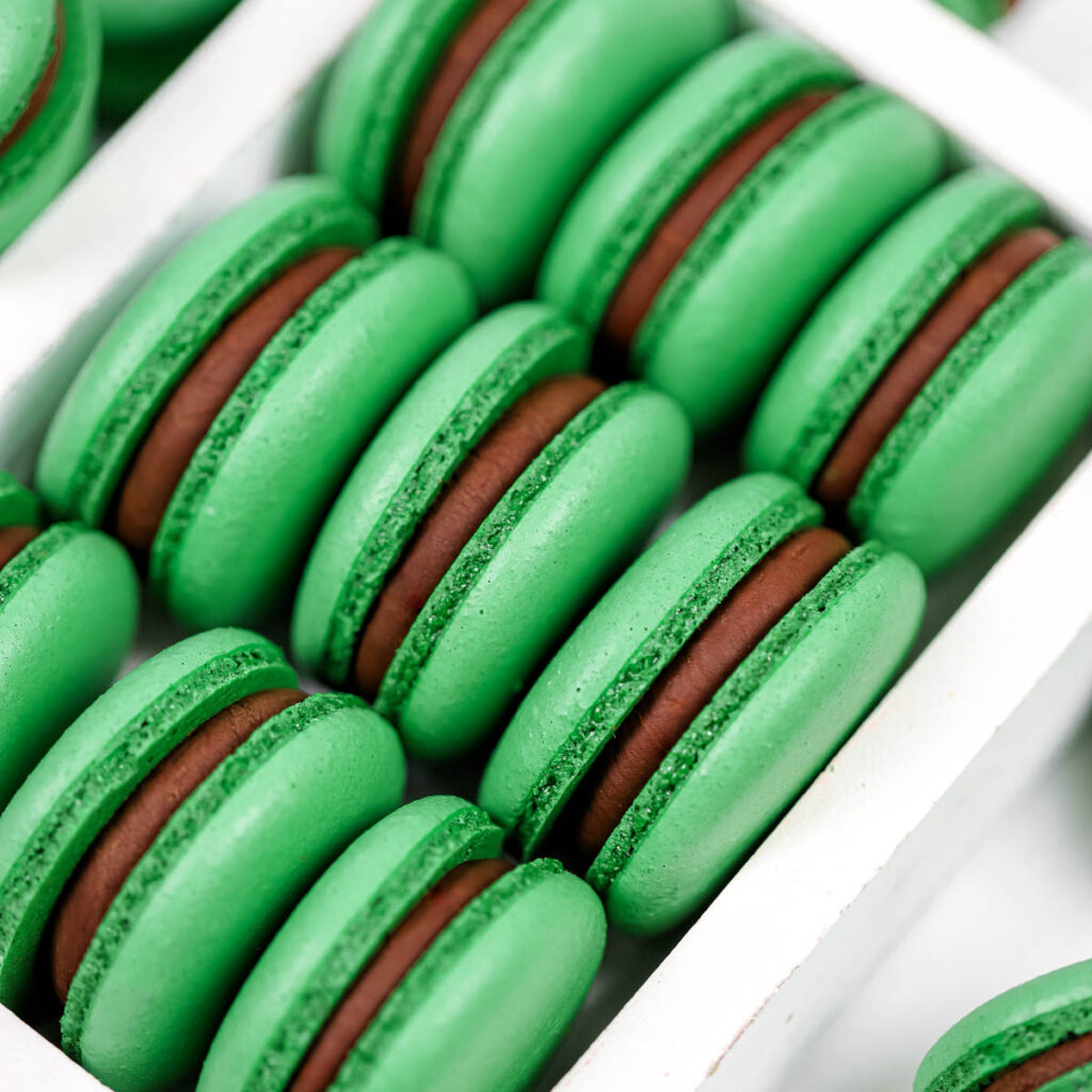 Green macarons filled with dark chocolate ganache in the box.