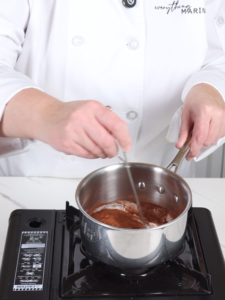 Saucepan with cream and cocoa powder. 