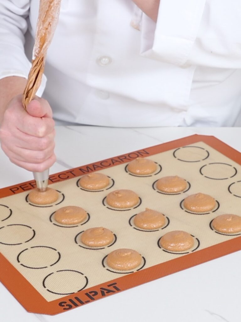 Piping macaron shells on the baking mat. 