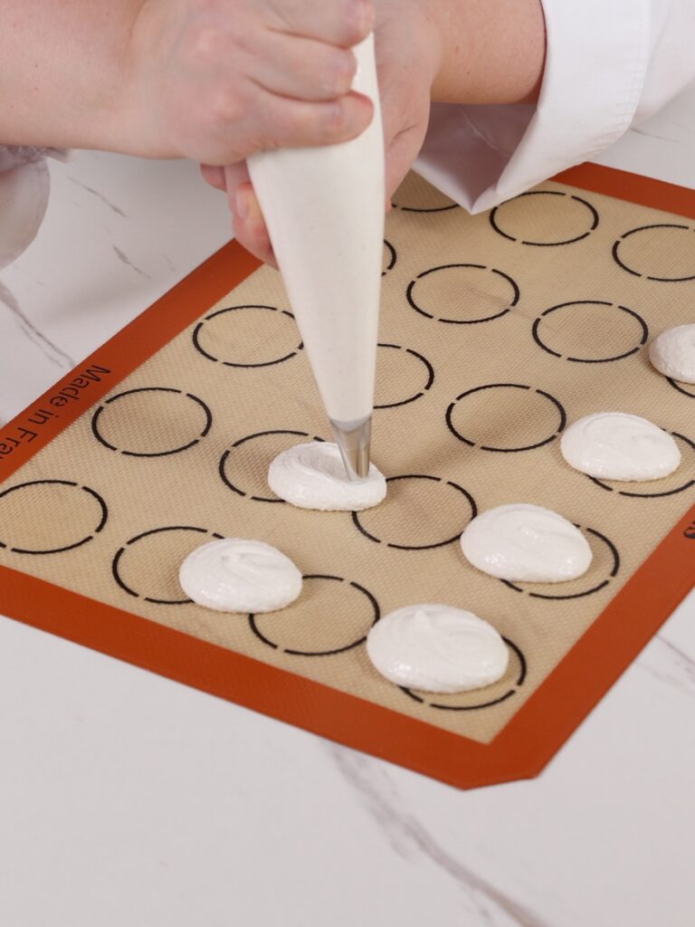 The hand is piping egg-shaped macarons. 