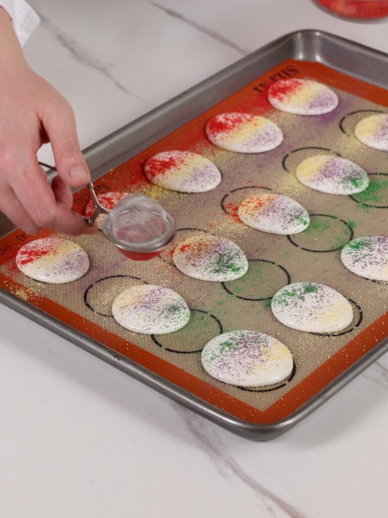 The hand is dusting macarons with the powder. 