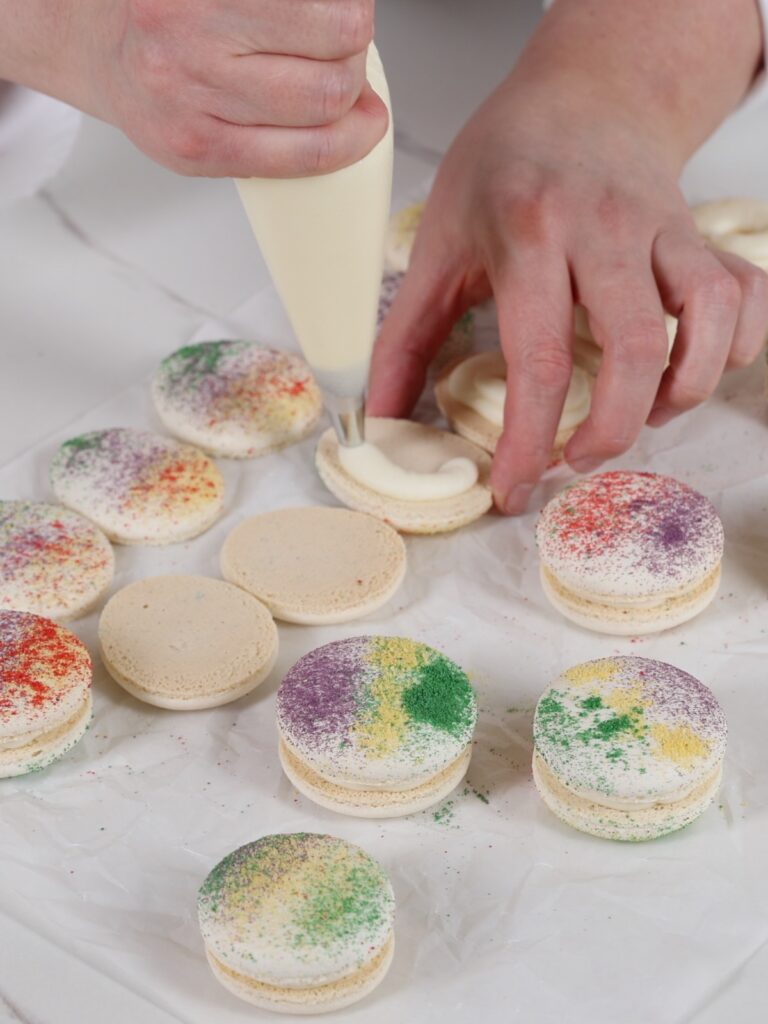 Hands are piping frosting on the macarons. 