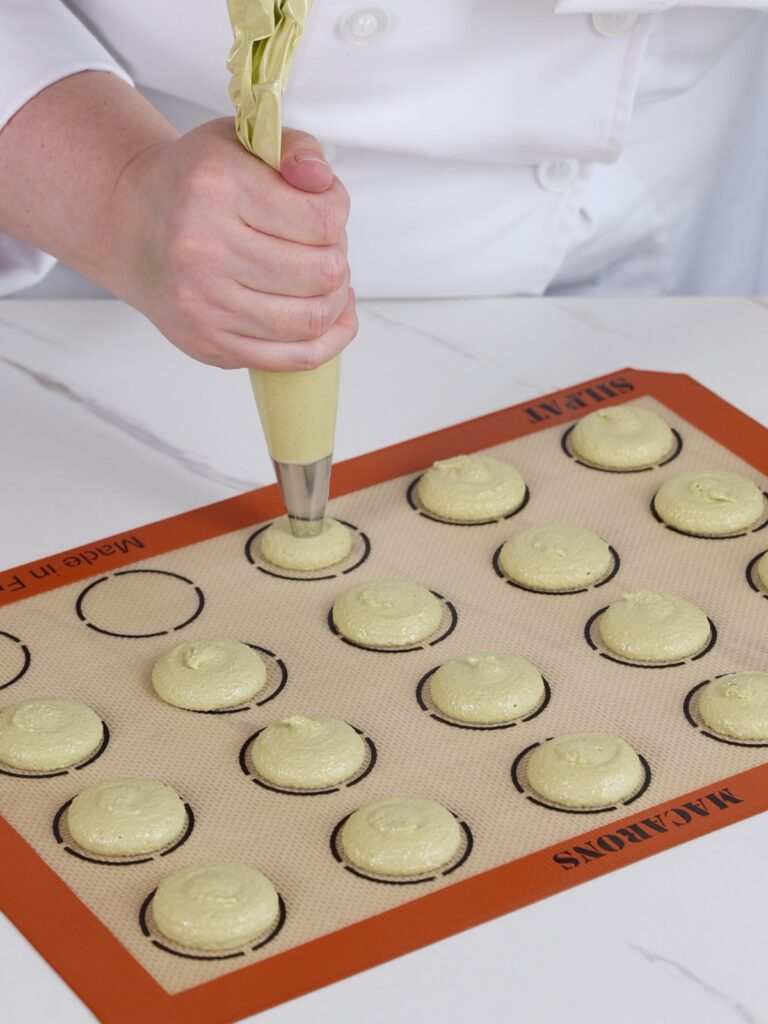 Piping macarons on the mat. 