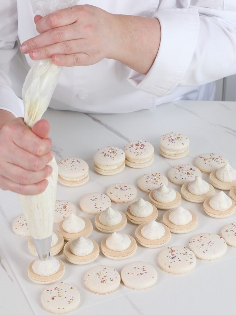 Piping whipped ganache on macaron shells. 