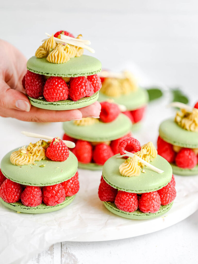 Hand holding Pistachio Ispahan Macarons. 