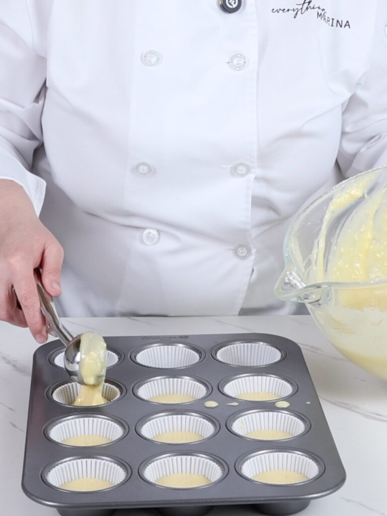 Pouring lemon cupcake batter into muffin tins. 