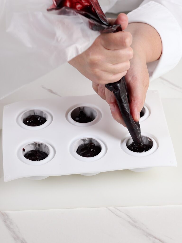Pipping blueberry filling into a silicone mold.