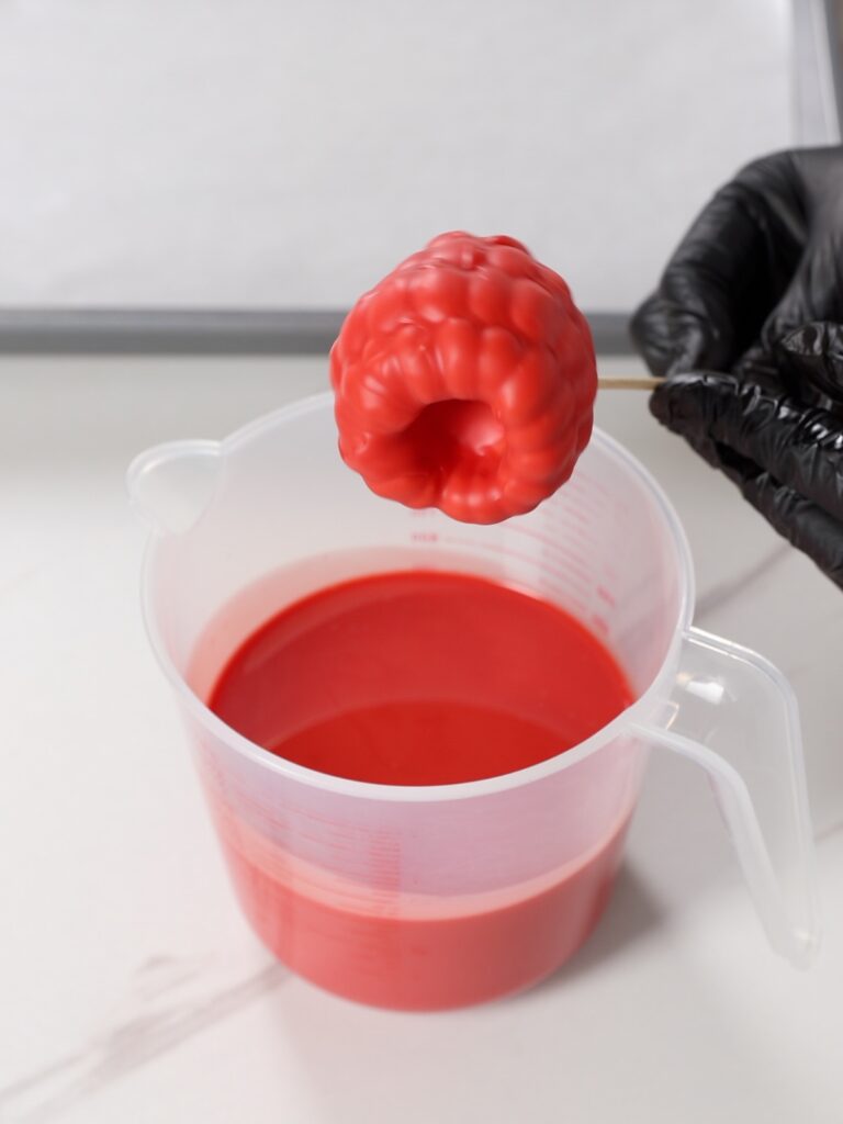 Dipping a raspberry into a chocolate coating.