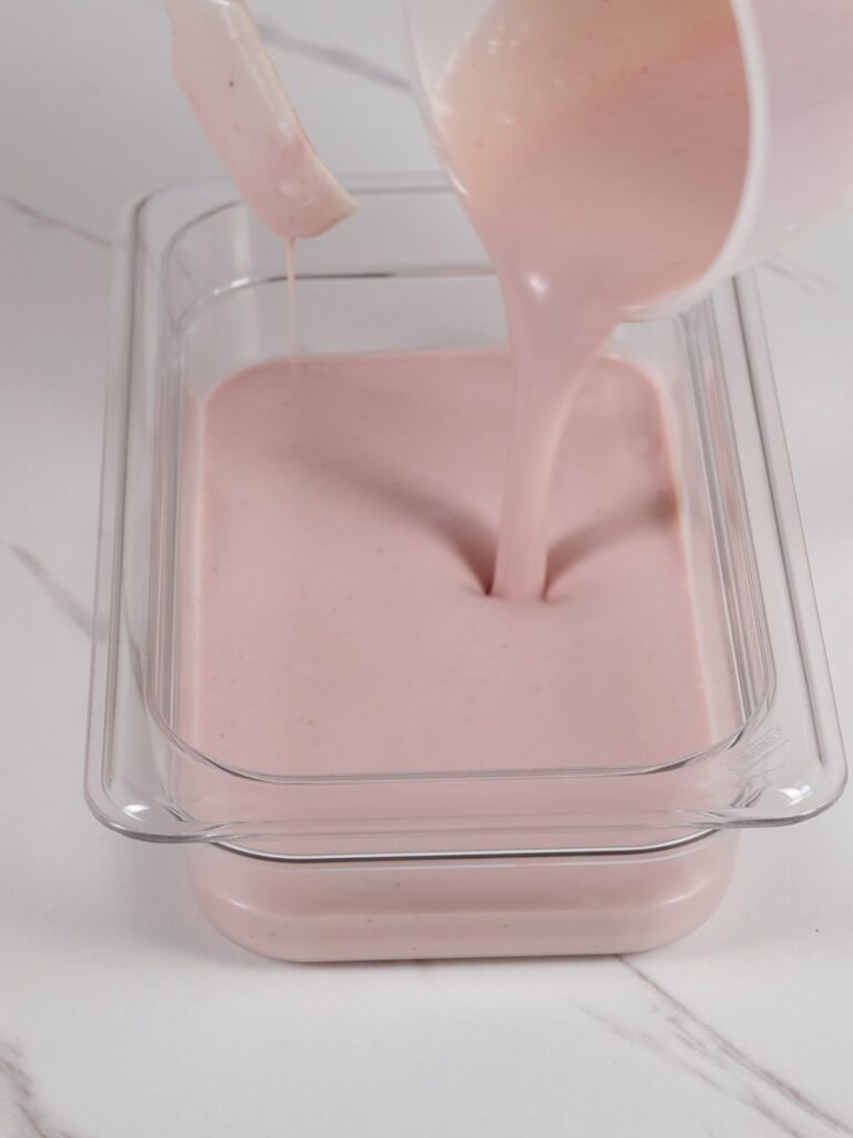 Pouring strawberry ganache into a flat container.