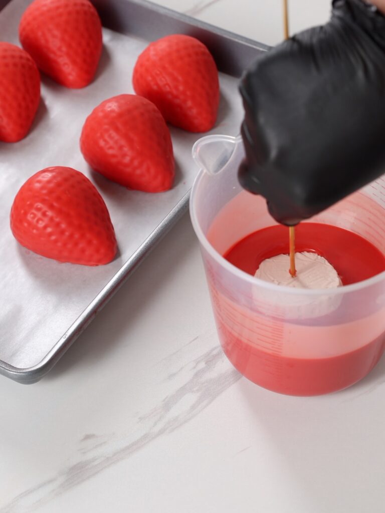Covering the strawberry in the chocolate.