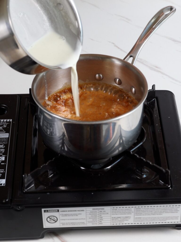 Pouring heavy cream into melted sugar in the saucepan.