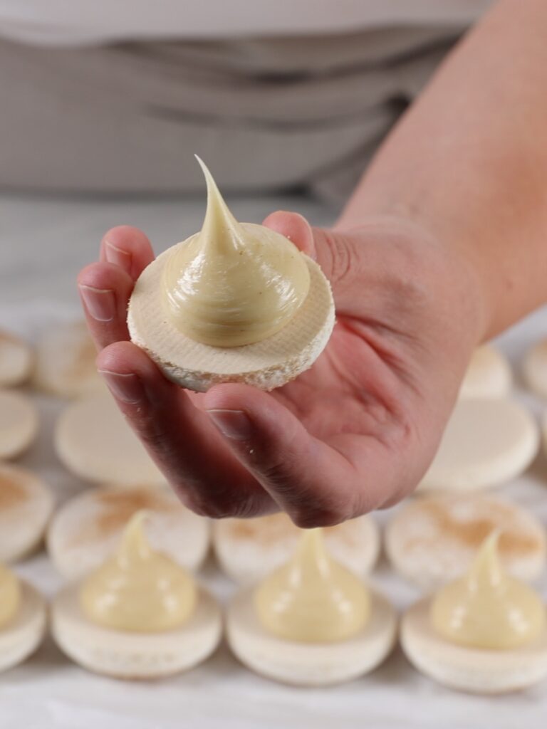 Cinnamon ganache is piped on the macaron shell. 