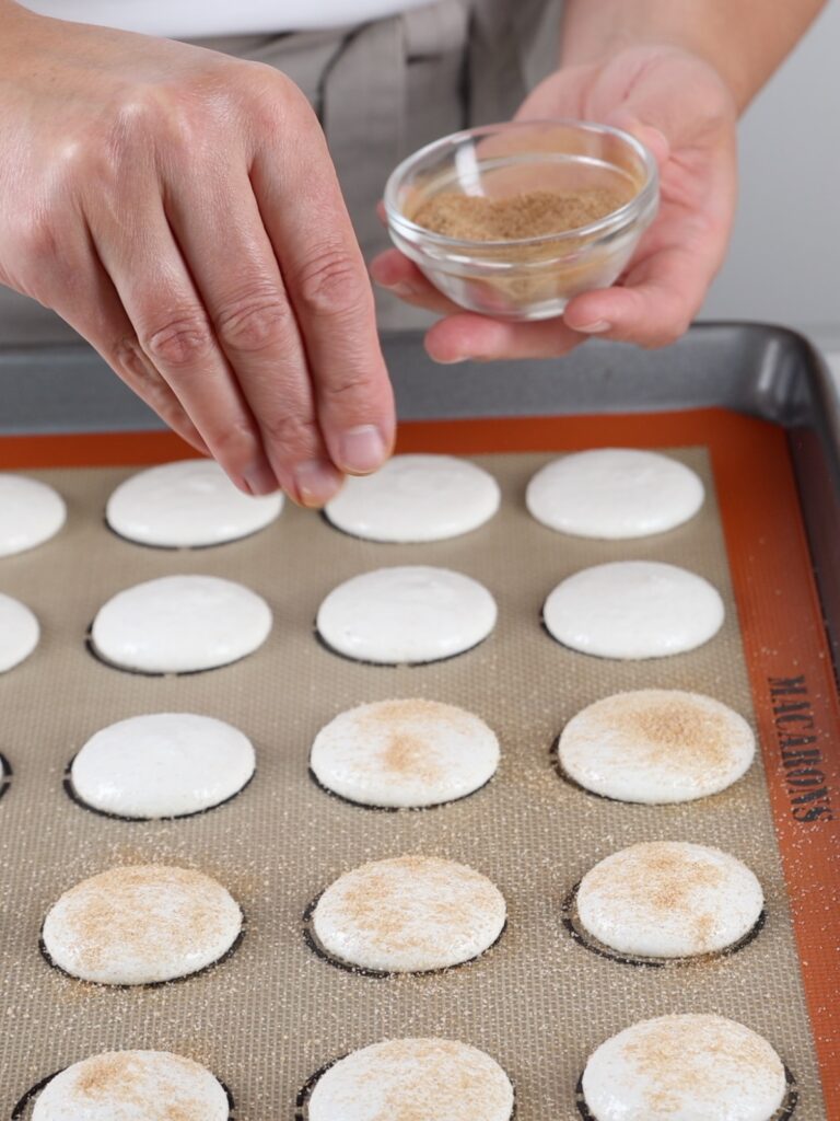 Hand sprinkling macaron shells with the sugar.